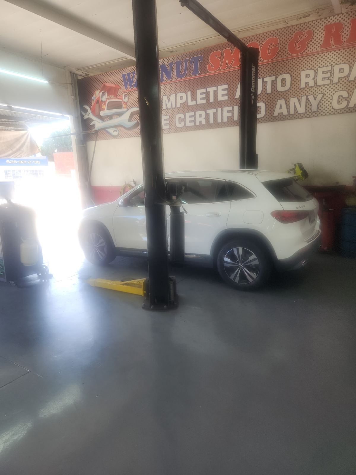 Inside Walnut Smog & Repair in Pasadena, CA, with the shop banner and a vehicle on the lift